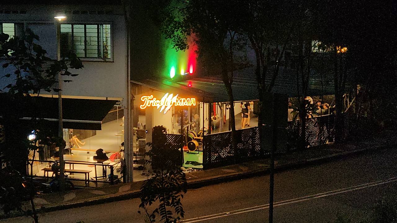 78 Rifle Range Road at night: the Tricolor MMA sign lit over the open ground-floor premises, with the street and trees in front.